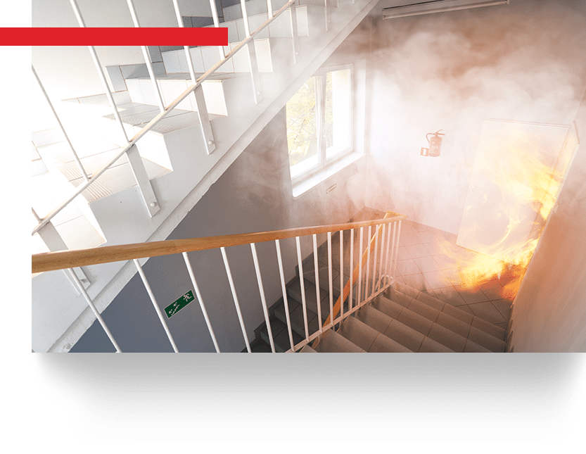 Escalier enfumé avec flammes sortant d'une porte, extincteur et signalétique de secours lors d'un incendie.